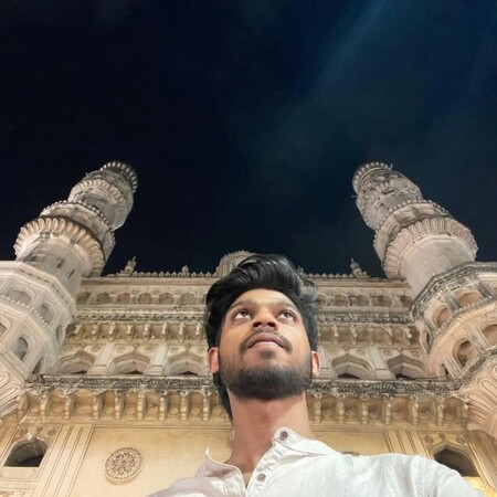 Man in a white shirt standing in front of an illuminated historic monument with two ornate minarets at night.