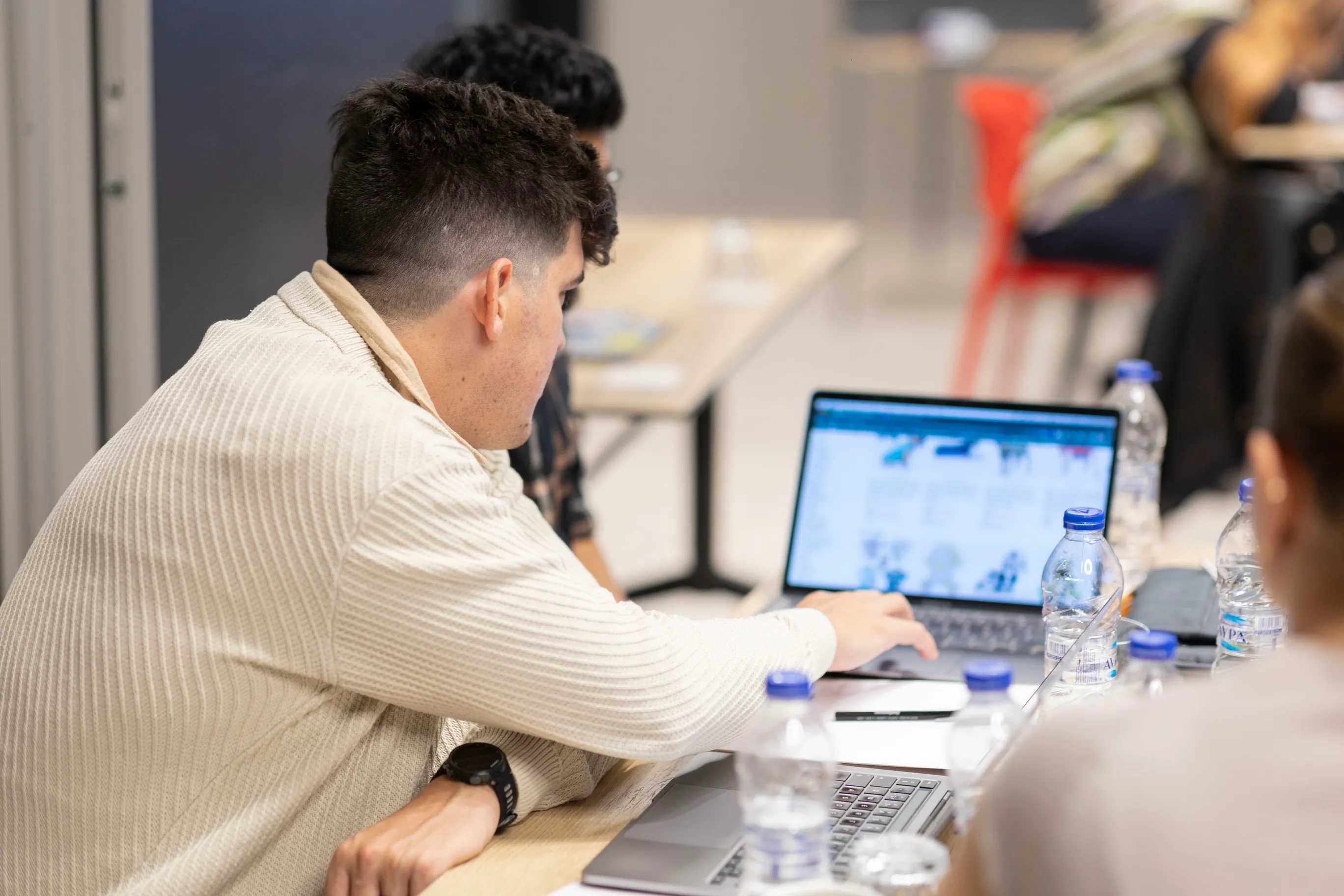 Two people collaborating and working on laptops at a table with water bottles.