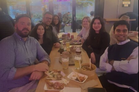 Group of six people sitting around a restaurant table with drinks and food, smiling at the camera.