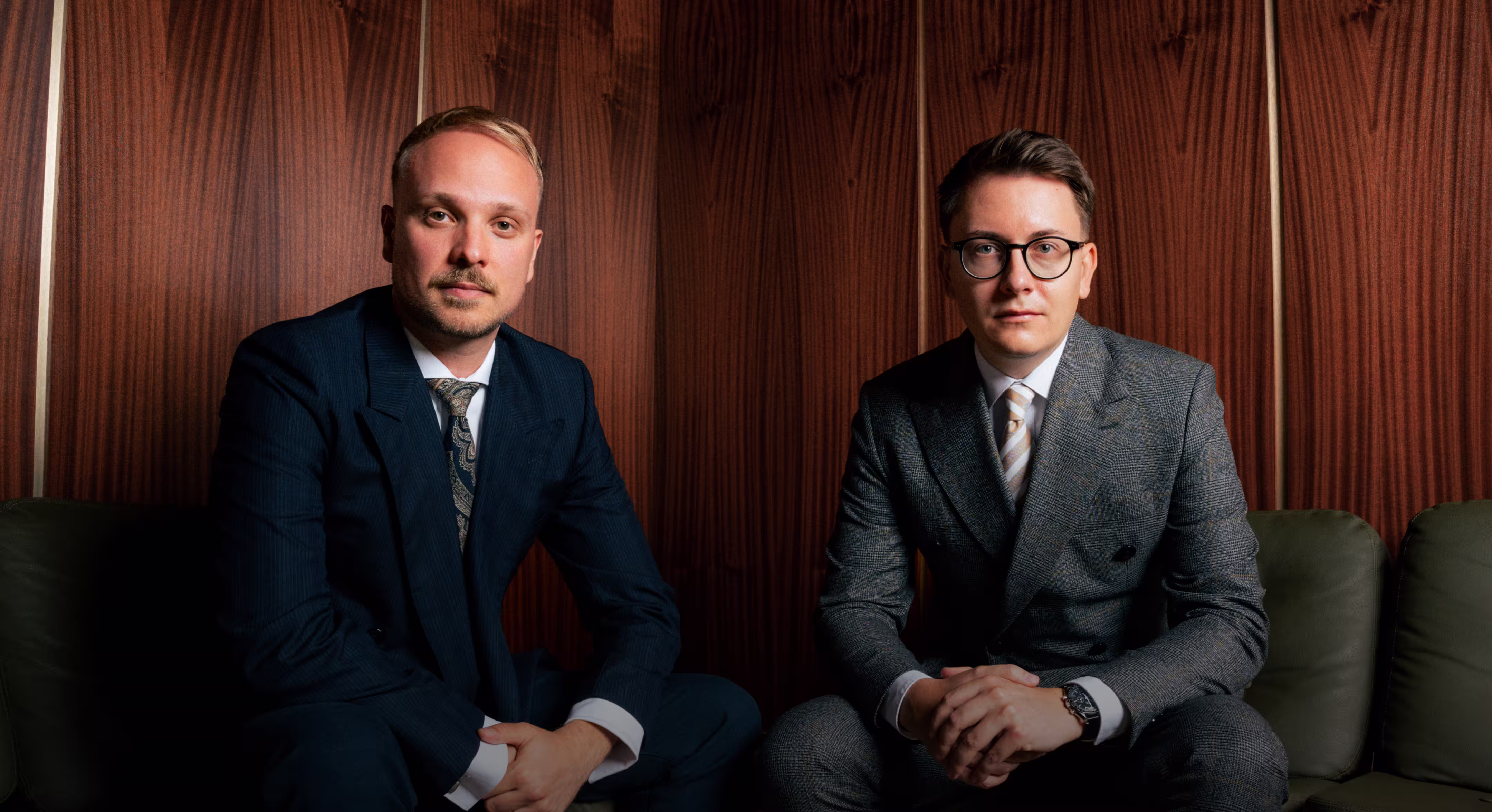 Foto im Breitbildformat, auf der linken Seite sitzt Rechtsanwalt Jonas Meese, auf der rechten Seite sitzt Rechtsanwalt Alexander Schlüter, beide sind in Anzügen gekleidet, im Hintergrund eine holzvertäfelte Wand