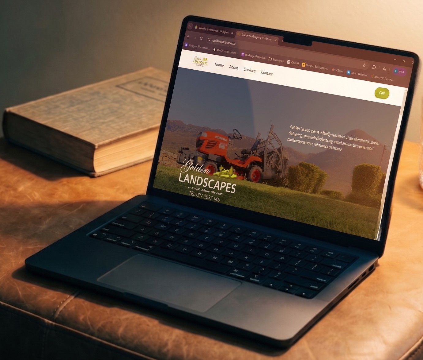 Open laptop displaying the Golden Landscapes website featuring a lawn tractor and trimmed bushes on a wooden surface with a closed book nearby.
