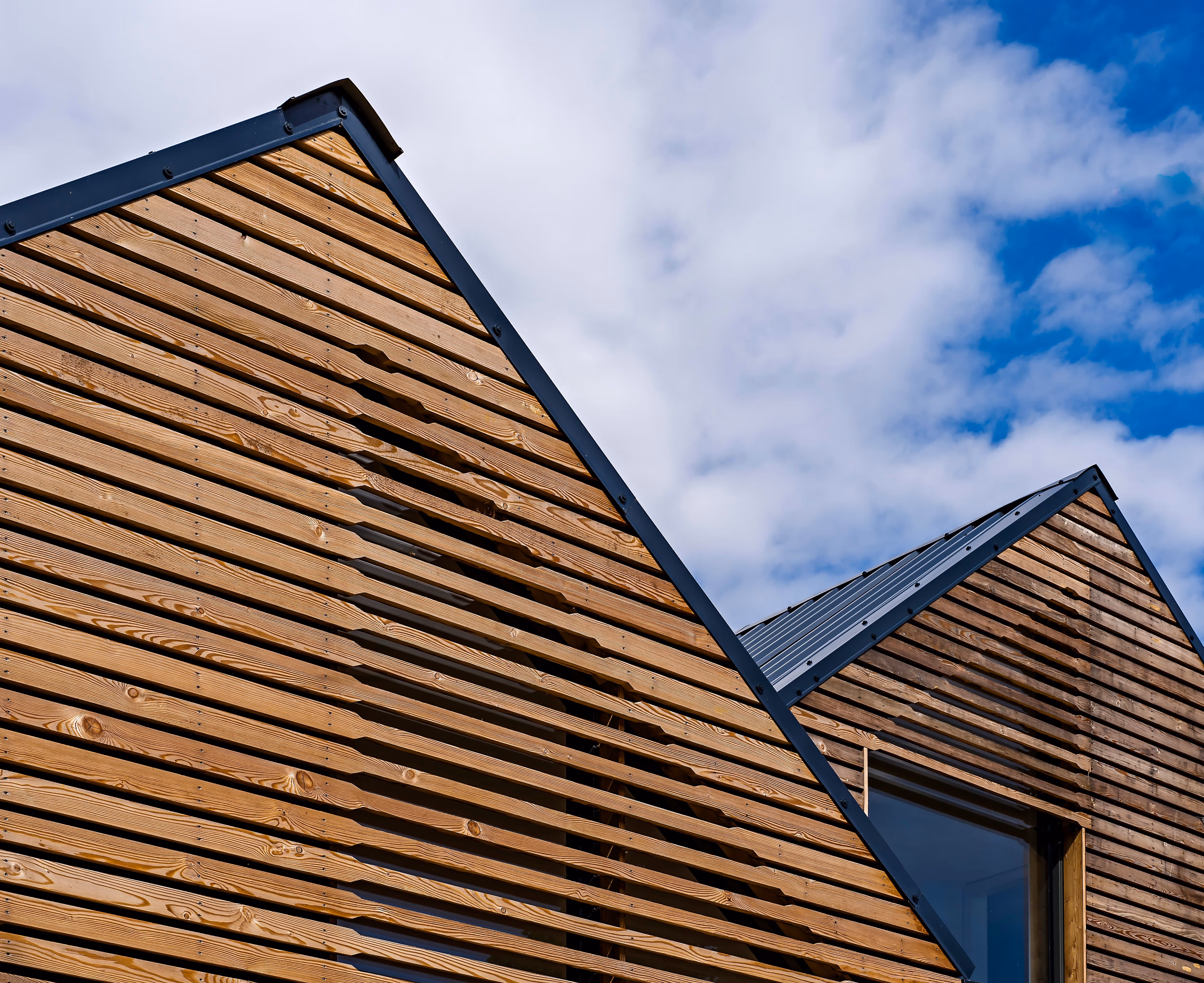 Close-up of modern wooden building facades with triangular roofs under a partly cloudy sky.