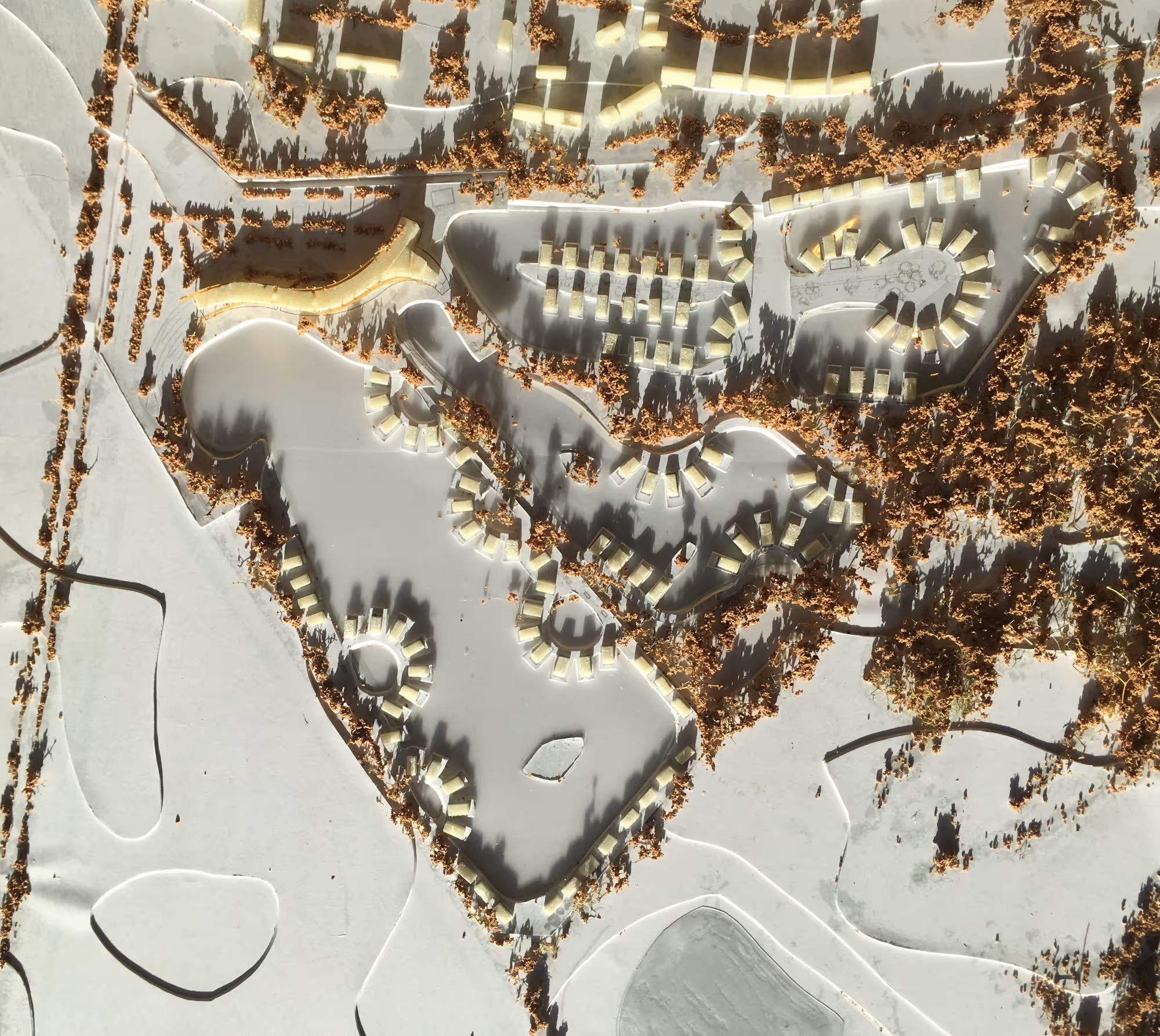 Architectural scale model of a residential area with curved roads, circular house clusters, and scattered trees casting shadows.