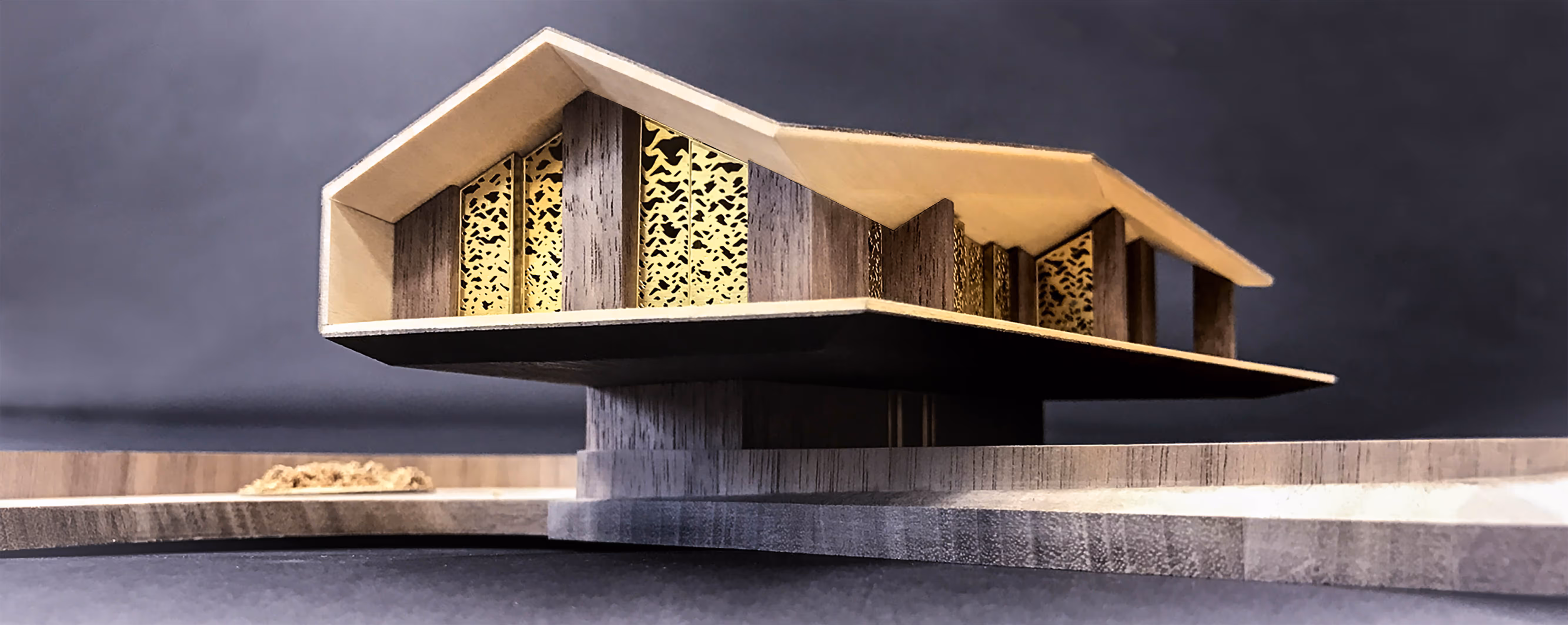 Architectural model of a modern building with a large cantilevered roof and decorative perforated panels, elevated on a cylindrical base.