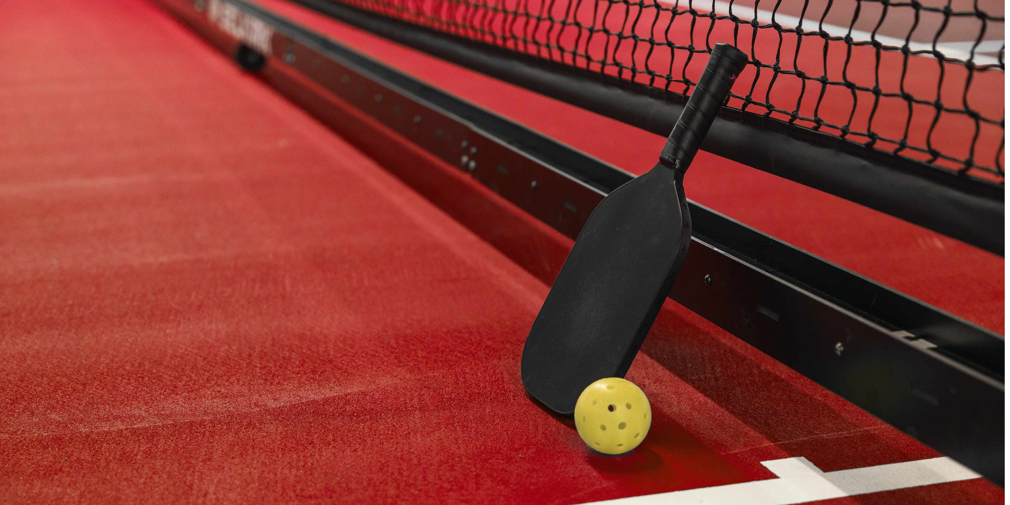 Pickleball Racket with a ball on Maroon Court