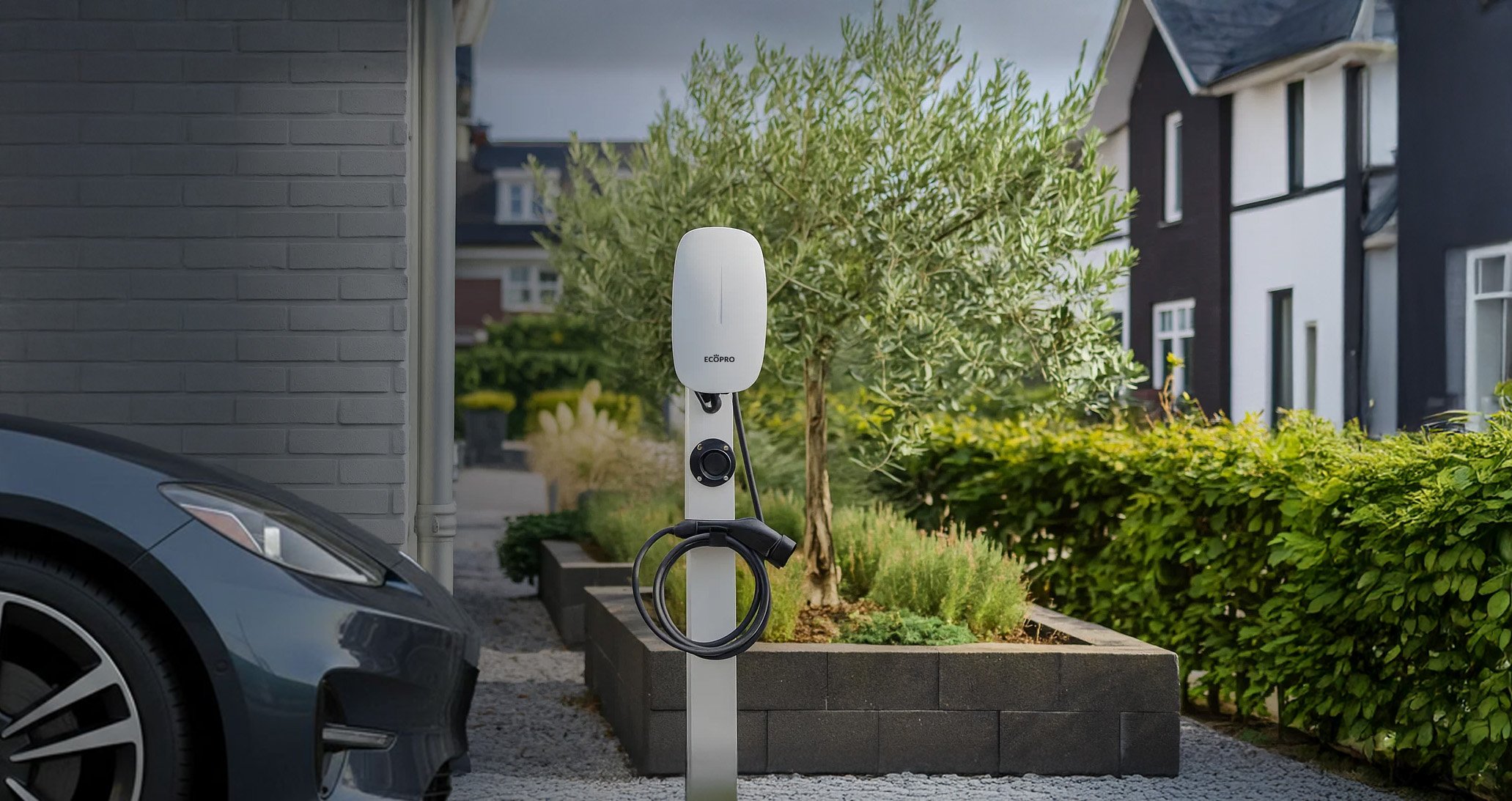 Electric vehicle charging station mounted on a post next to a black car parked by a modern house with greenery.