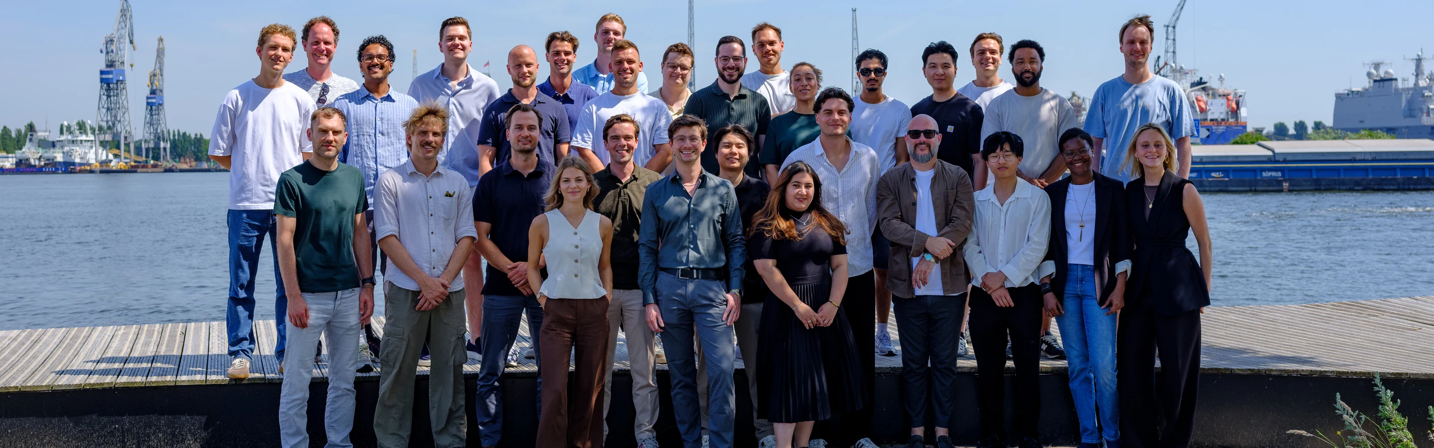 The Cargoplot team standing together on the quayside at Danzigerkade in Amsterdam, with harbour cranes and ships behind them.