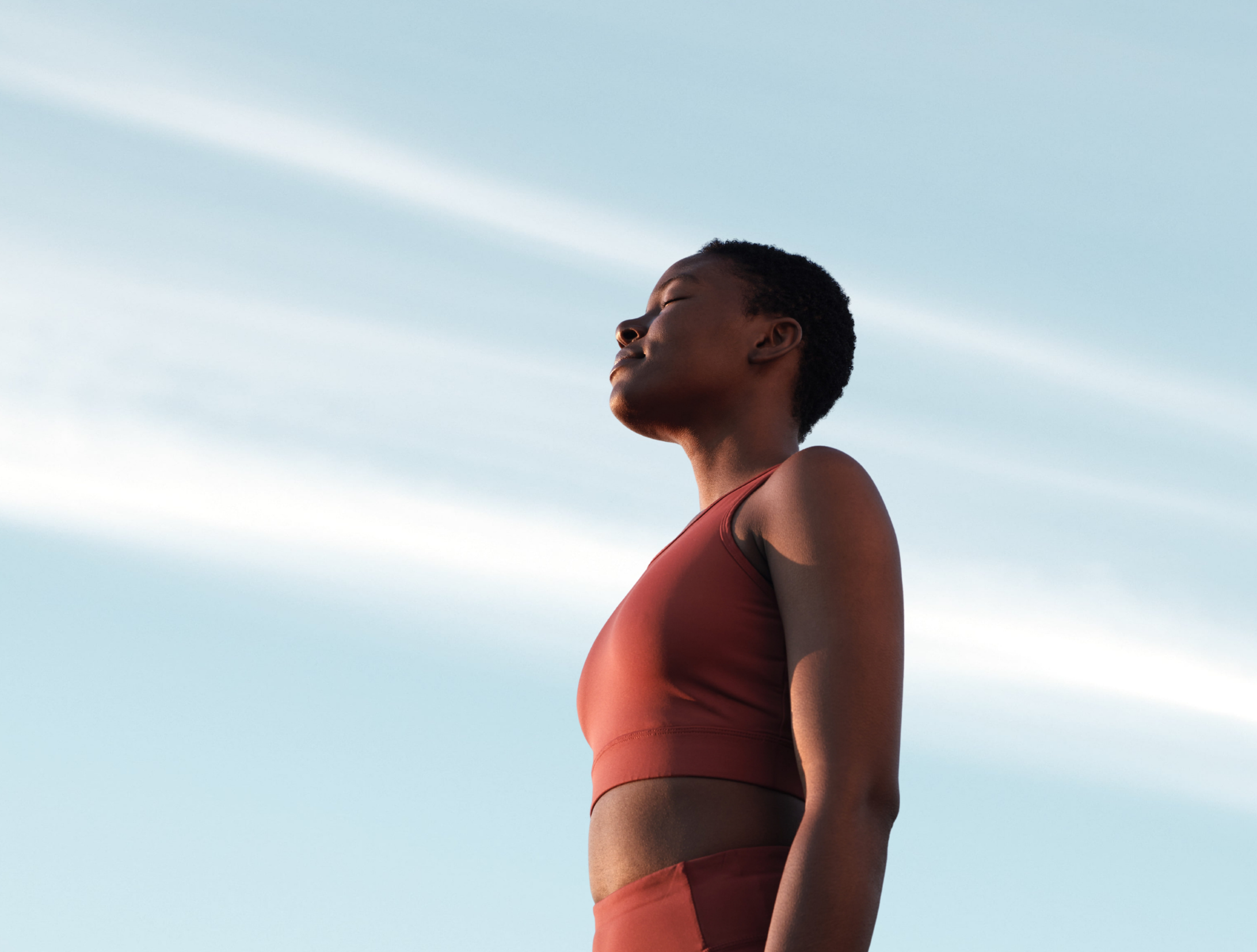 Person in a red tank top standing outdoors with eyes closed.