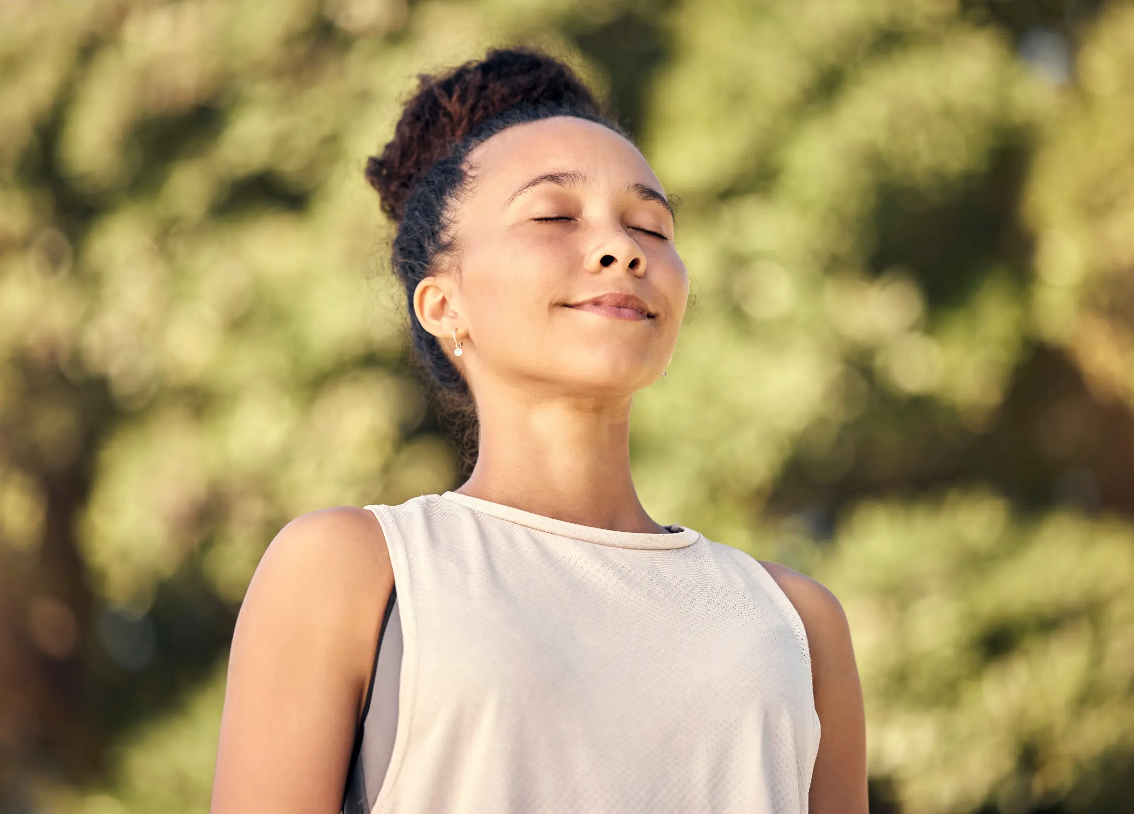 A young woman with her eyes closed, smiling peacefully outdoors in natural sunlight.