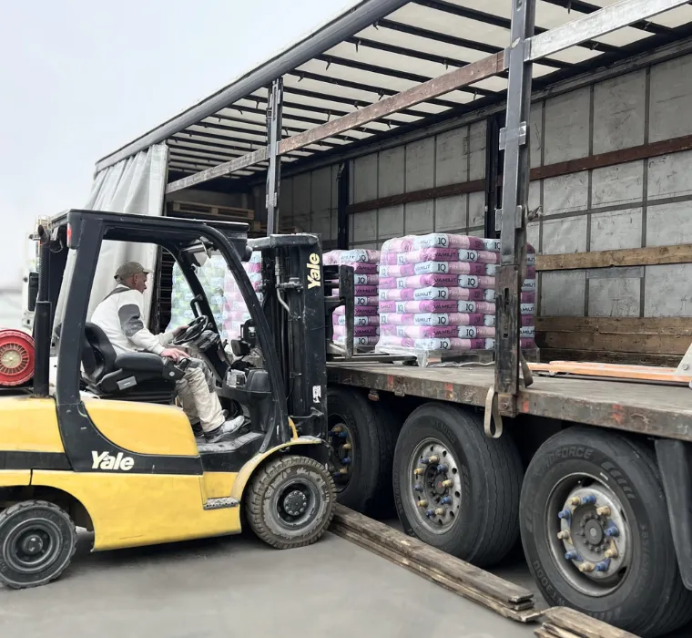 Людина на вантажній міні машині вивантажує у вантажівку сухі будівельні суміші