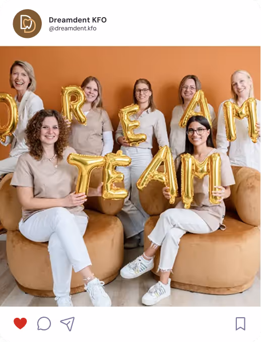 Ein Team von sieben Mitarbeiterinnen hält goldene Luftballon-Buchstaben, die das Wort ‚Dream Team‘ ergeben, und sitzt lächelnd in einer freundlich gestalteten Praxis mit orangener Wand.