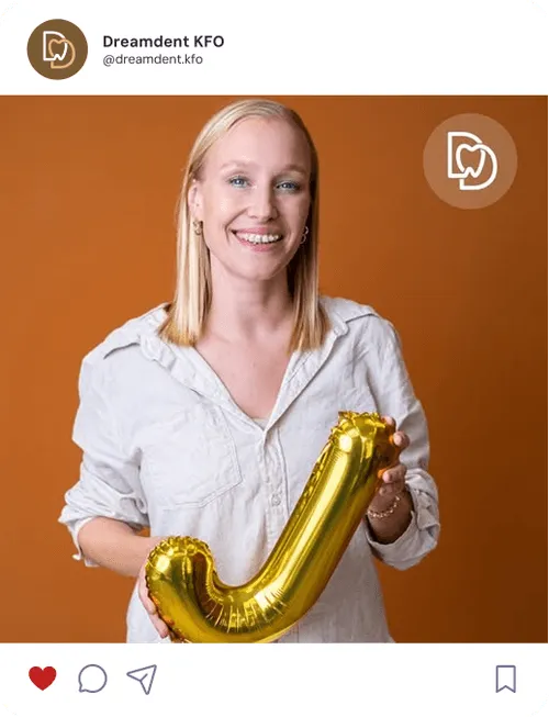 Eine lächelnde Frau steht vor einer warmen orangefarbenen Wand und hält einen goldenen Luftballon in Form des Buchstabens J.