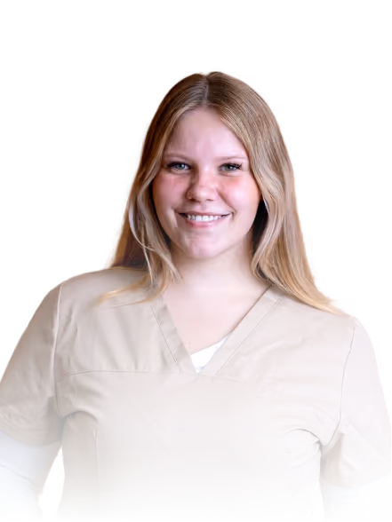 Junge Frau in beiger medizinischer Arbeitskleidung lächelt freundlich vor dunklem Hintergrund.