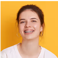 Lächelnde Jugendliche mit Zahnspange vor gelbem Hintergrund – moderne Kieferorthopädie und sanfte Zahnkorrektur bei DreamDent Family.