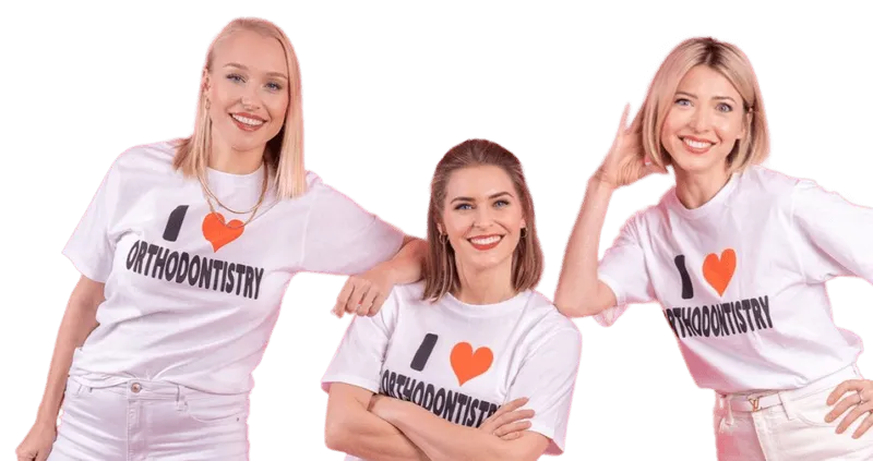 Drei lächelnde Frauen in weißen T-Shirts mit der Aufschrift ‘I ❤️ Orthodontistry’, posierend vor dunklem Hintergrund.