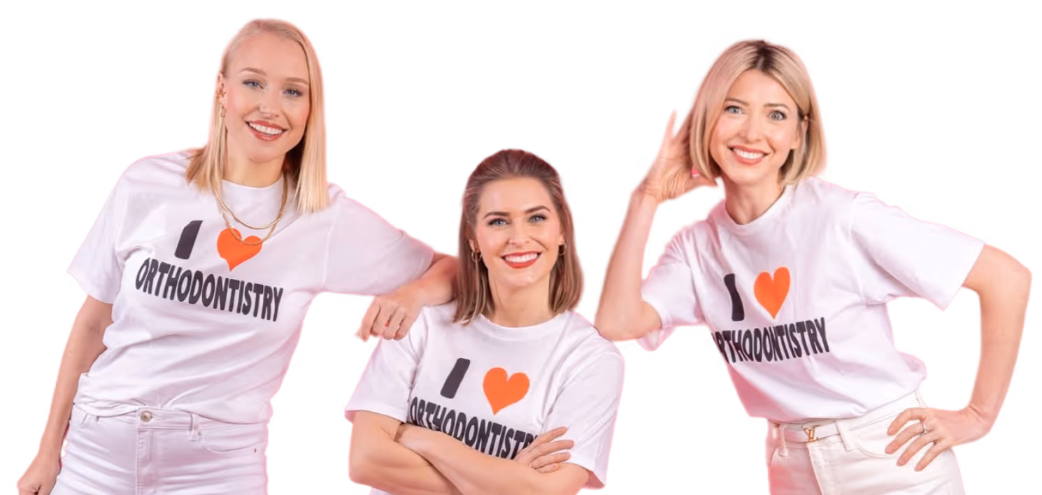 Drei lächelnde Frauen in weißen T-Shirts mit der Aufschrift ‘I ❤️ Orthodontistry’, posierend vor dunklem Hintergrund.