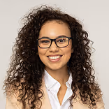 Smiling woman with curly hair and glasses wearing a beige blazer and white shirt.