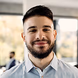 Smiling man with a beard and short dark hair wearing a light blue collared shirt.