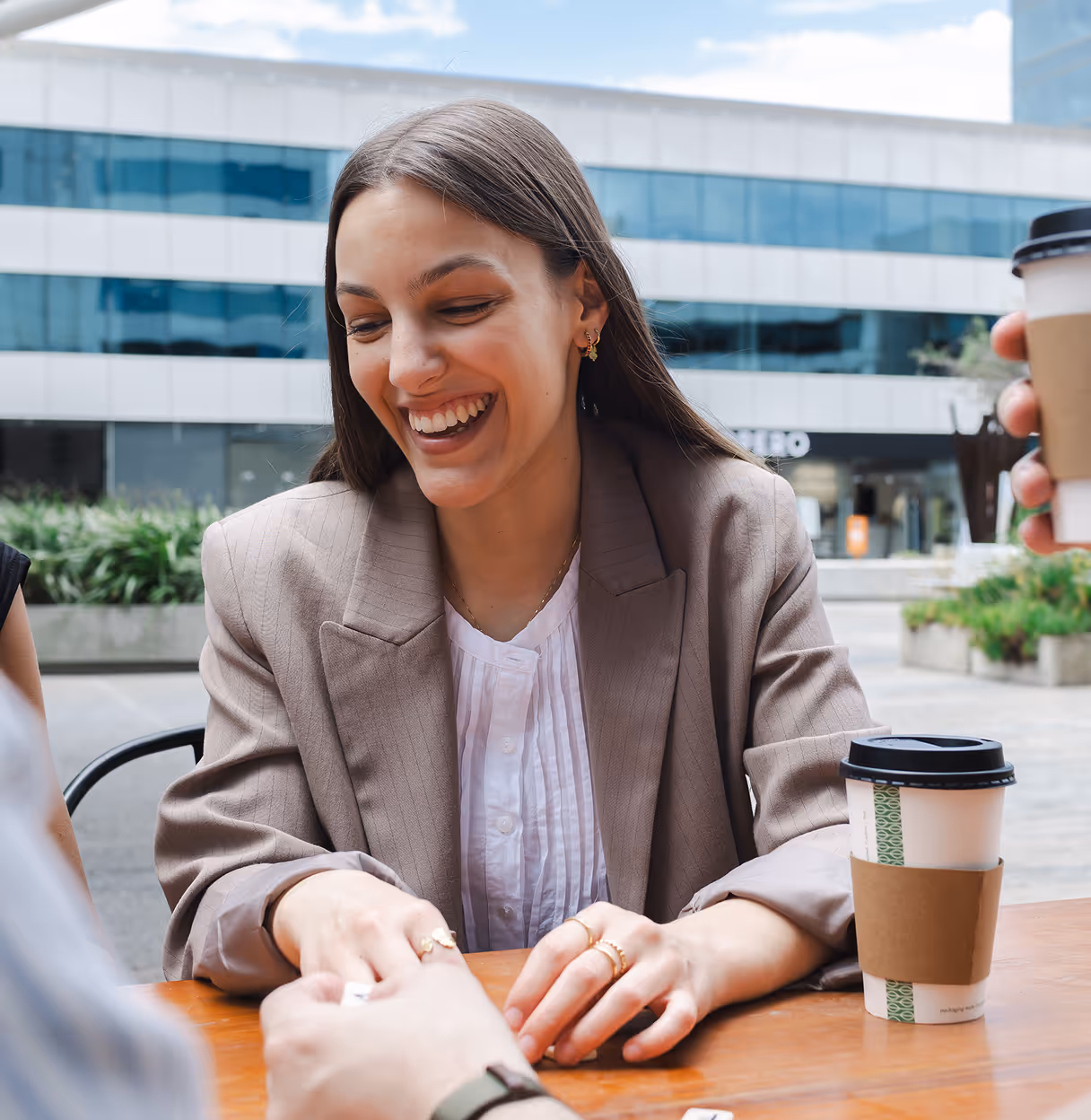 Smiling woman in a blazer playing a table game outdoors with coffee cups on the table.