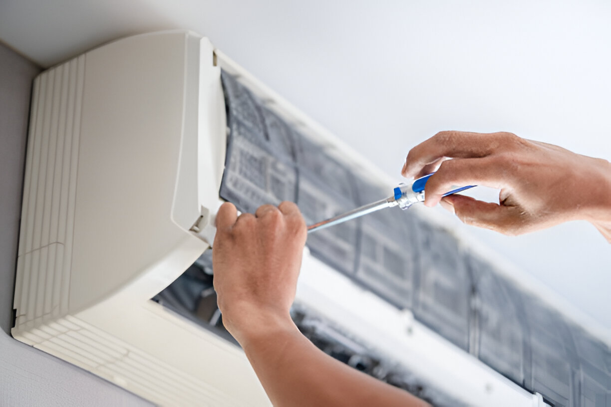 A technician repairs an air conditioner unit using a screwdriver for maintenance.
