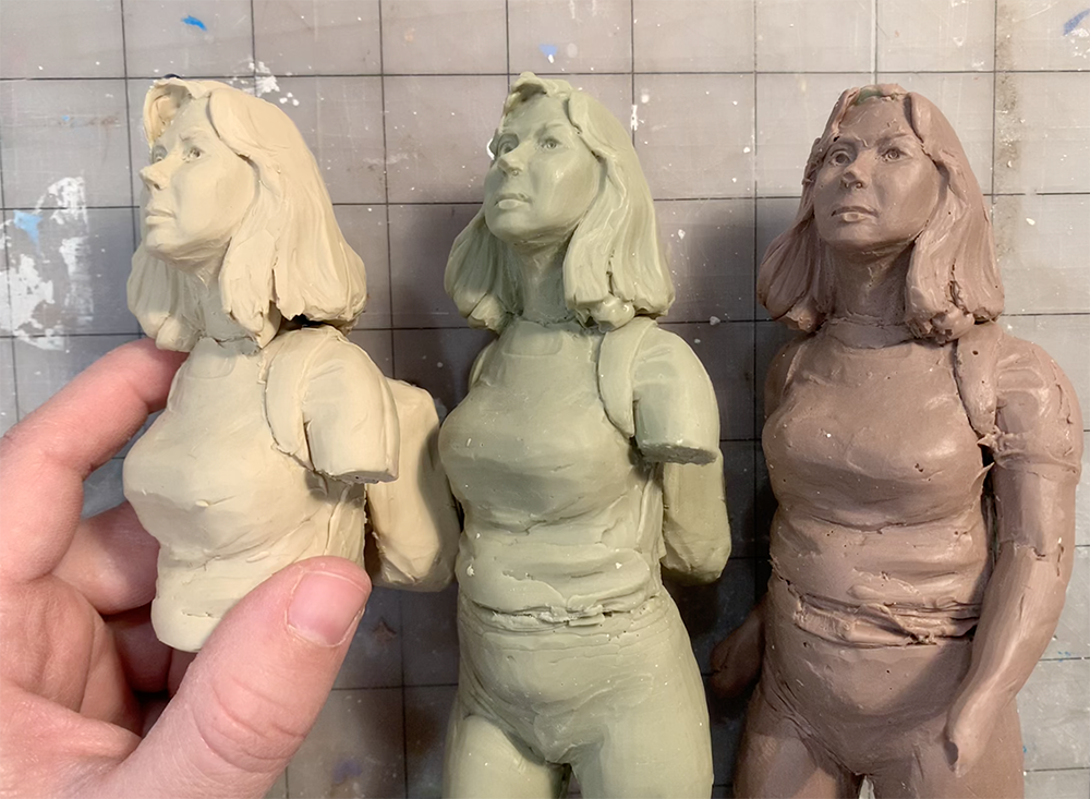 Three small clay figure maquettes in grey, green and terracotta, held in the artist's hand — a modelling study from the Projections project. Links to the Experiments gallery.