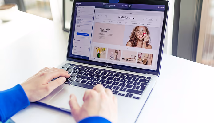 Person using a MacBook Pro laptop displaying a natural beauty product website with a smiling woman holding a pink makeup sponge.