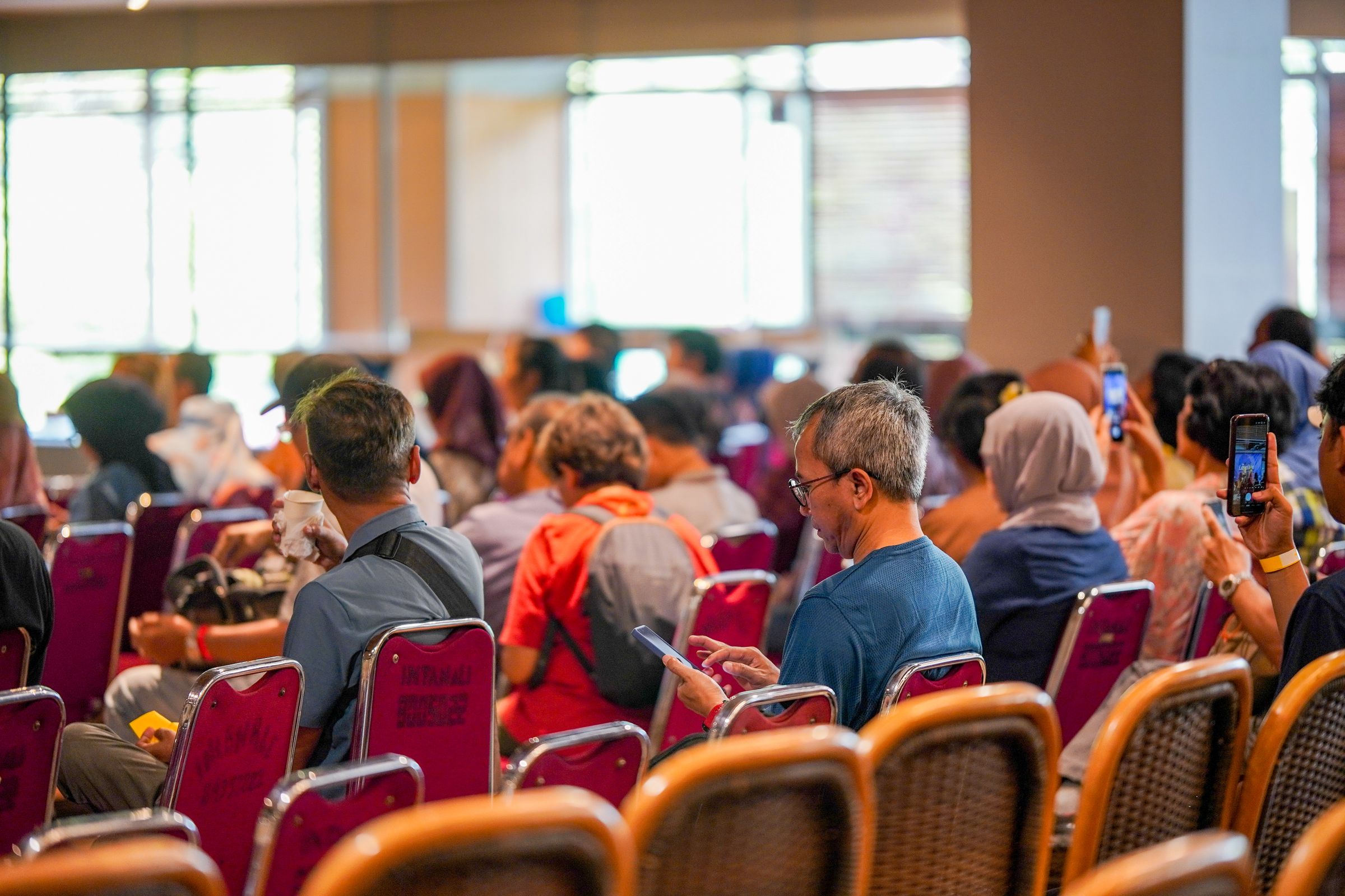 Attendees seated in a conference hall, several of them using their phones