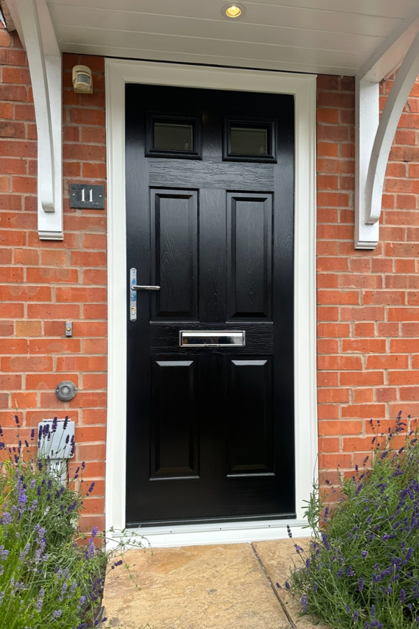Front black wooden door with silver handle and mail slot set in a red brick wall with house number 11 and lavender plants on either side.