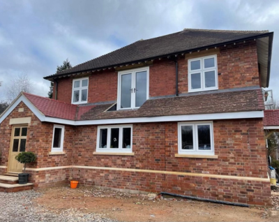 Two-story red brick house with multiple white-framed windows and a cloudy sky overhead.