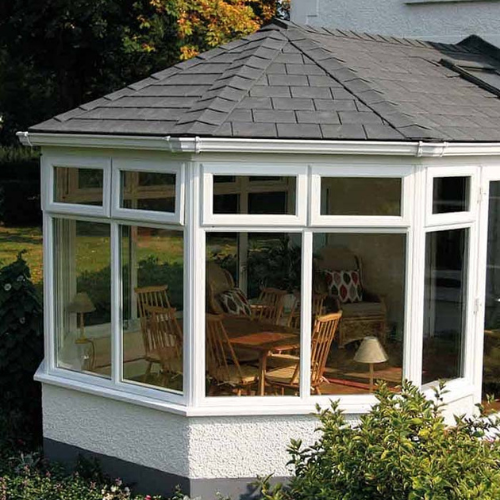 Sunroom with white framed windows, a gray shingled roof, and wooden table and chairs inside.