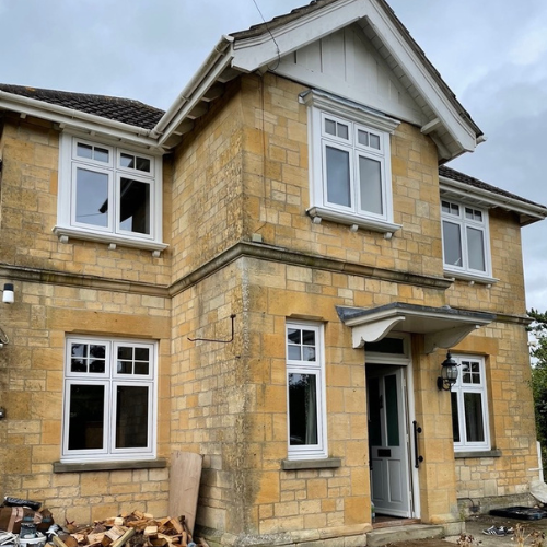 Two-story stone house with white framed flush sash windows and a white front door under a small porch.