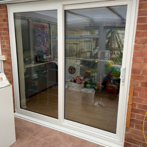 White sliding glass door revealing a sunroom with children's toys and laundry appliances inside.