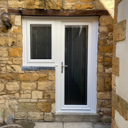 uPVC white framed glass door with an adjacent small white window set in a rustic stone wall.