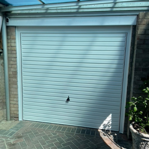 Closed white garage door with horizontal panels, surrounded by brick walls and a tiled driveway.