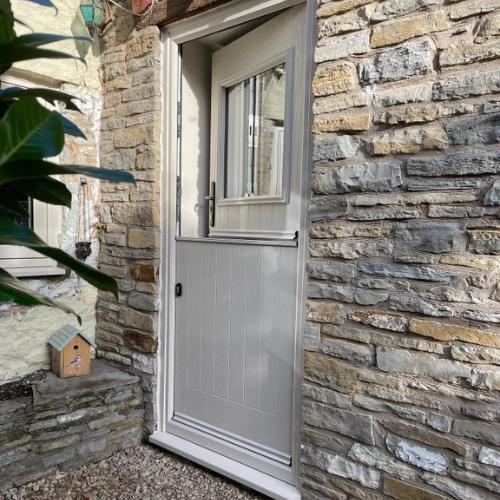 Half-glass grey composite stable door set in a Cotswold stone wall with a small birdhouse on a stone ledge nearby.