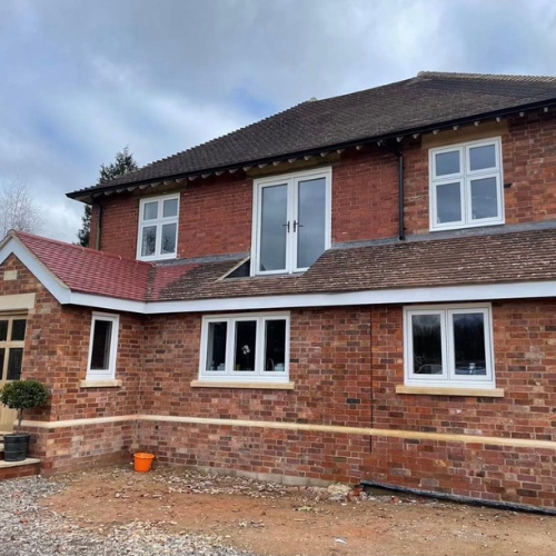 Two-story brick house under construction with white-framed Residence Collection windows and a door on the upper level without a balcony.