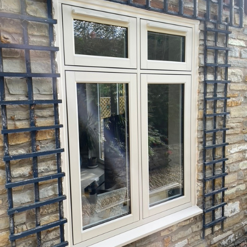 White framed Residence Collection window with clear glass set in a rustic stone wall with black metal trellis structures on either side.