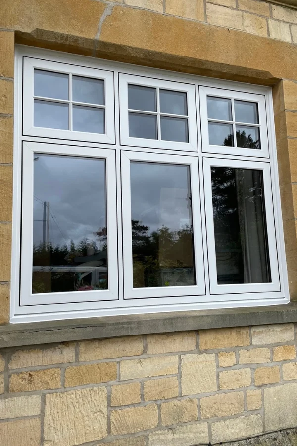 White uPVC window with three tall panels below and three smaller divided square panels above, set in a stone wall.
