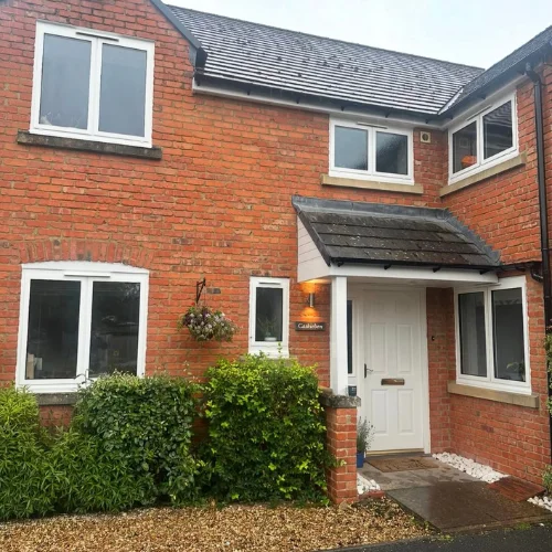 Two-story red brick house with white aluminum windows and a white front door under a tiled roof canopy.
