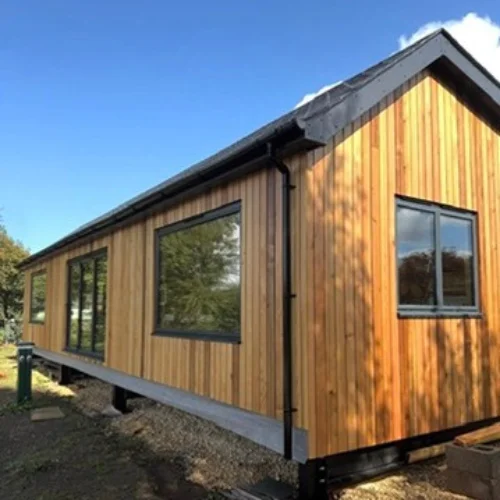 Modern wooden house exterior with black aluminum-framed windows under a clear blue sky.