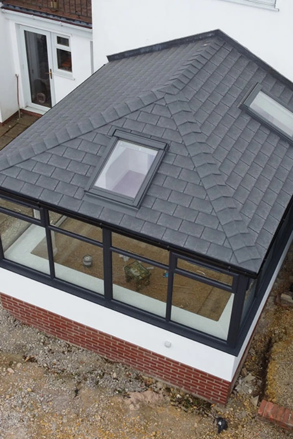 A modern conservatory with a grey tiled roof featuring two roof lights and large black-framed windows on a white and brick base.