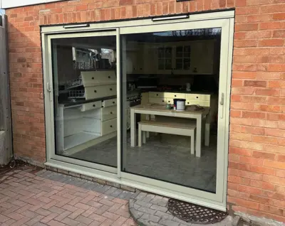 Green sliding patio door installed in a brick wall, showing a kitchen interior with white cabinets and a small table.