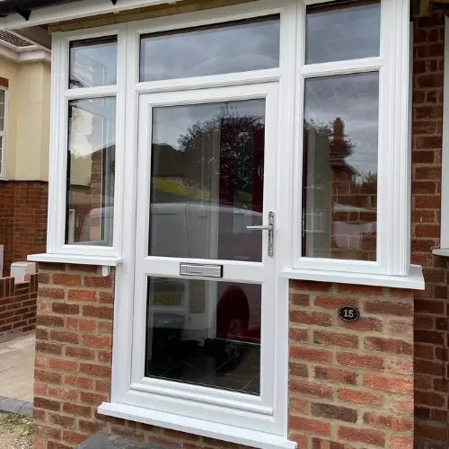White UPVC front door with glass panels set in a brick porch with two side windows and a black house number 15 plaque.