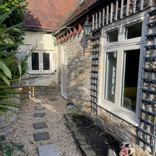 Stone cottage exterior with white-framed flush upvc Residence Collection windows, a gravel path with stepping stones, and greenery on the side.