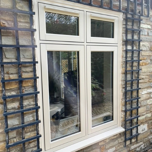 Double-pane cream-coloured flush uPVC Residence Collection window set in a stone wall with black metal trellises on each side.