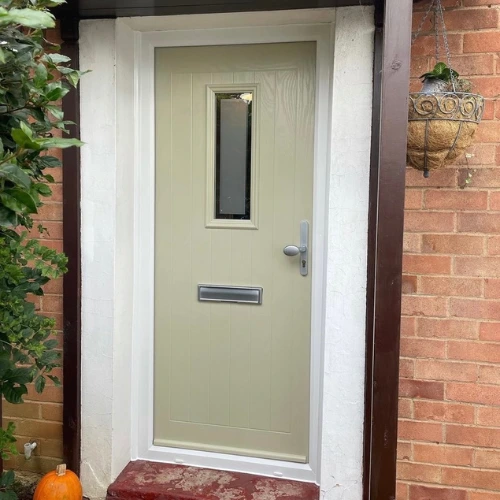 Light green front door with a vertical rectangular window and a silver mail slot, framed by white walls and brick exterior.