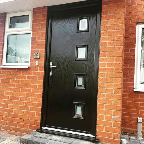 Black composite front door with four small square windows set in a red brick house with white-framed windows.