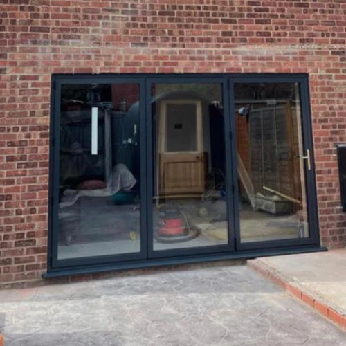 Black aluminum bifold doors installed in a brick wall opening leading to an indoor space under construction.