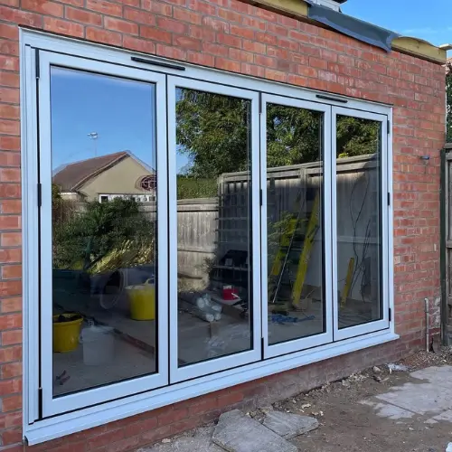 Modern white aluminium bifold doors installed in a red brick wall reflecting an outdoor garden and house.