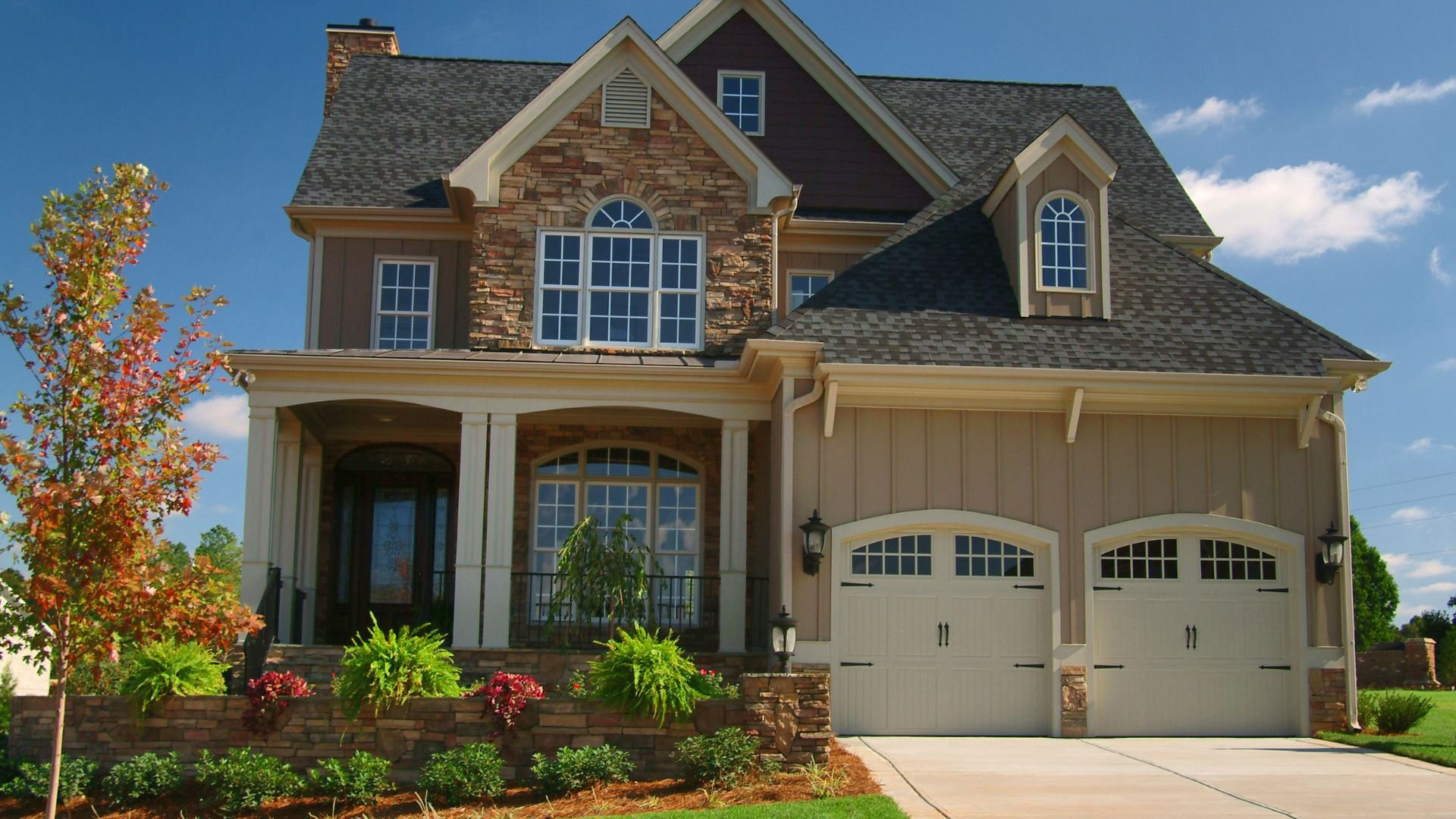 Two-story stone and wood house with double garage and autumn tree